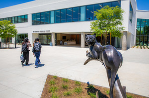 Two students walking on Rinker Campus on a sunny day, near the panther statue.