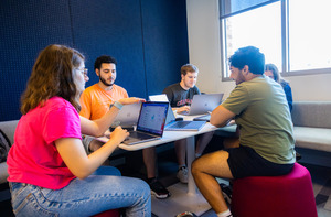 A group of students studying together using laptops in a small alcove area.