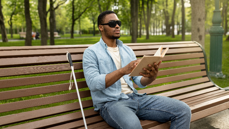 A blind student with a book sitting on a bench.