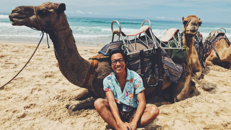 Chapman University student sits in sand in front of camel while studying abroad