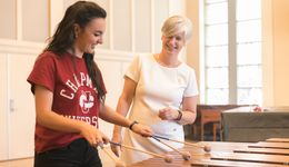 A student plays marimba while a professor looks on.