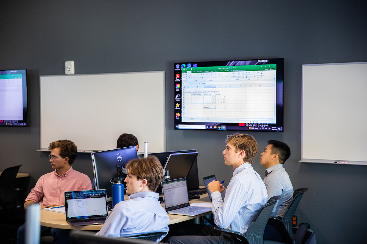 Chapman University students sitting at table with professor working on a tablet together