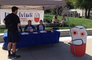 Students run an on-campus booth for the Rethink campaign. There is a standee of a cartoon pill next to the booth.