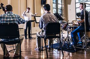 Three students play instruments while a professor conducts