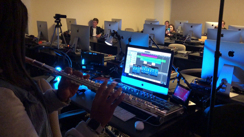 flute player stands in front of a monitor in music technology class