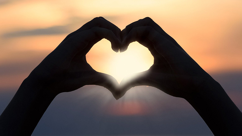 Two hands forming a heart with a sunset in the background