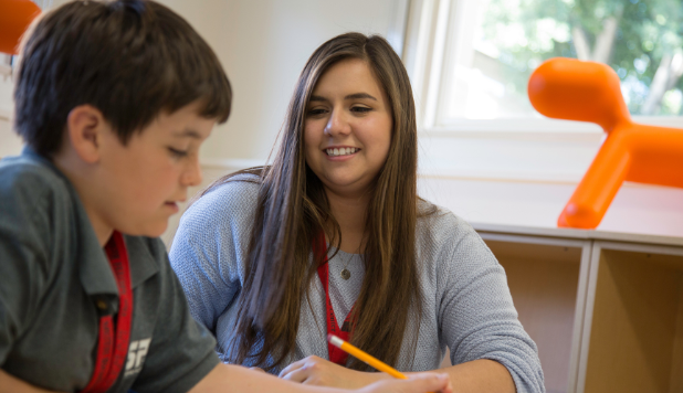 A student teacher works in an elementary aged student in a classroom.