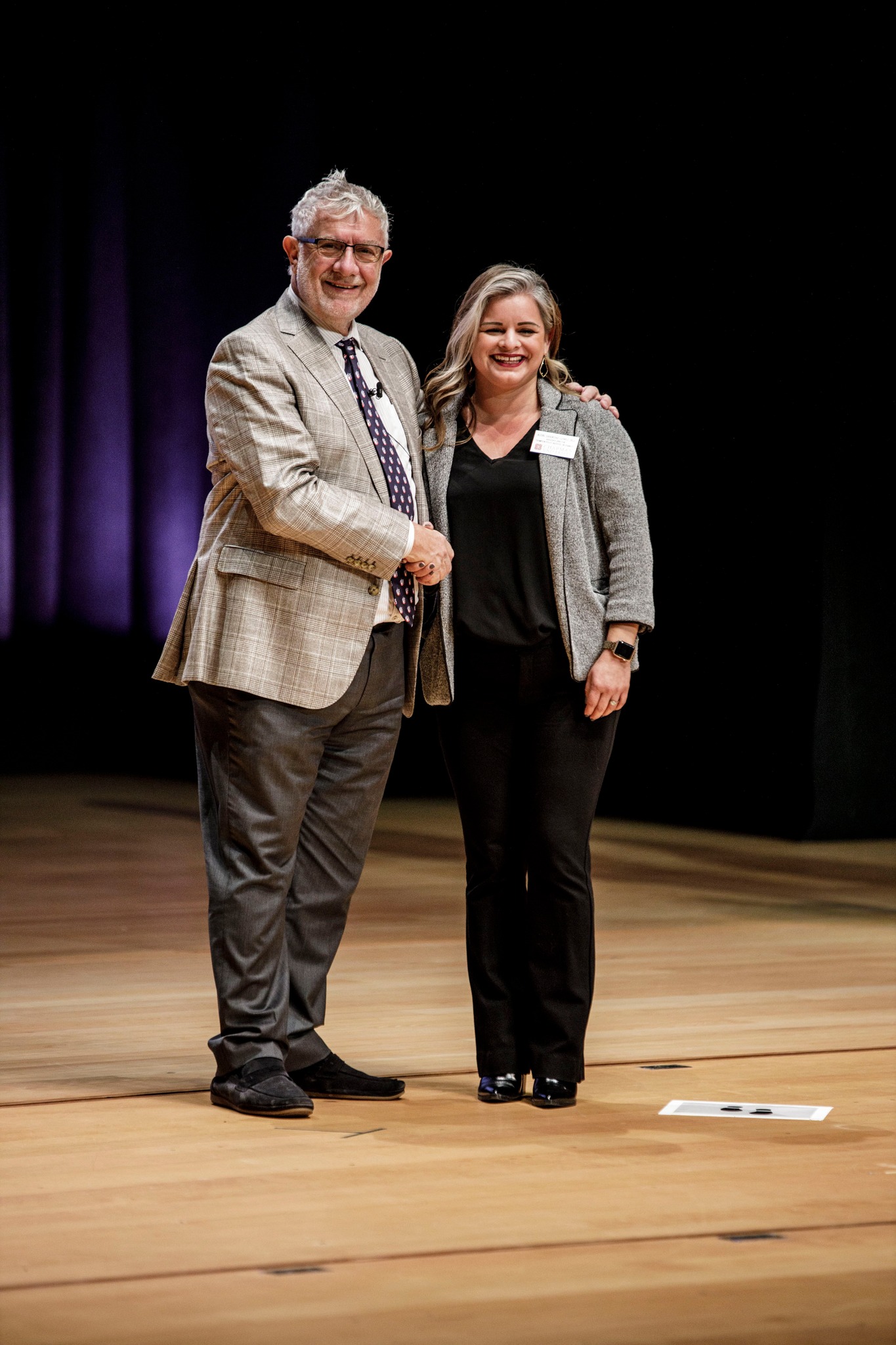 Dr. Gomez is standing on stage shaking the hand of Chapman University President Daniele C. Struppa, Ph.D.