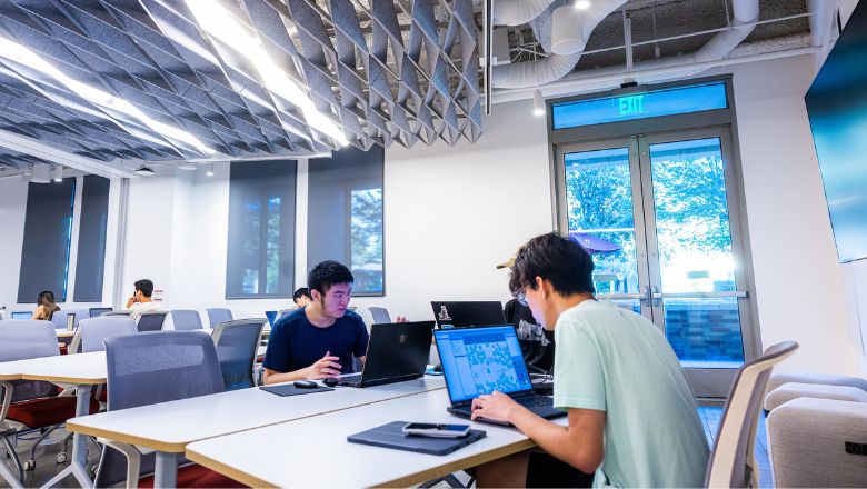 Two students sitting across each other on their laptops. 