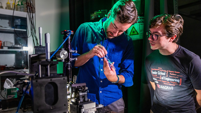 A student and faculty member examine a device in a lab.