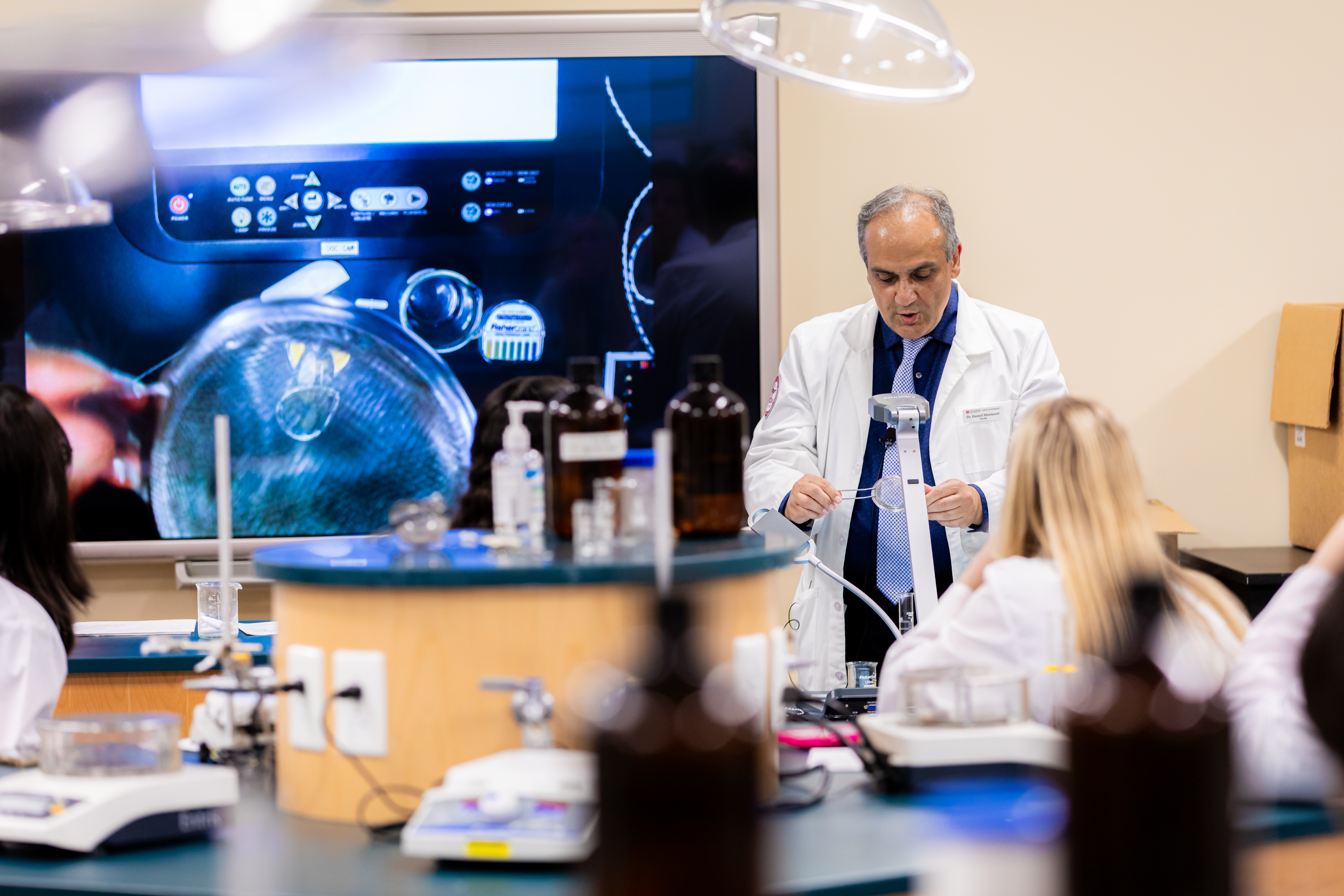 A man lecturing in the front of a lab with a lab coat on