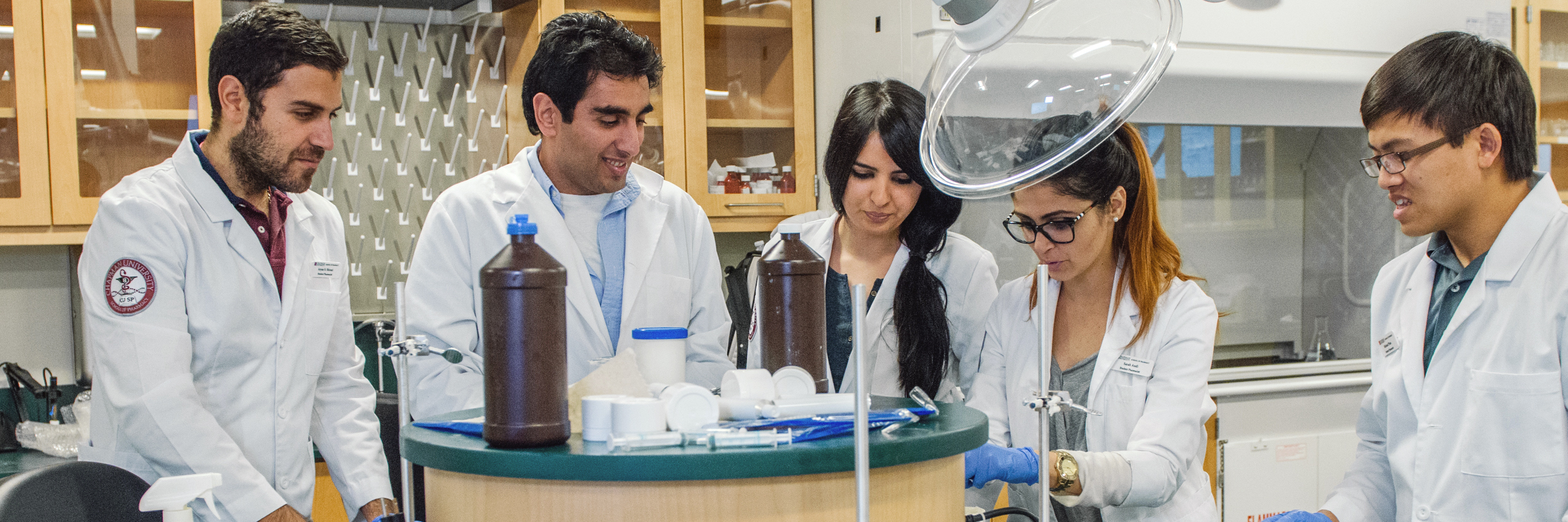 Two Chapman University students in white coats sit at desk in lab looking at computer screen