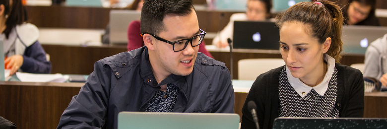 Two Chapman University students sit in lecture hall and look at laptops