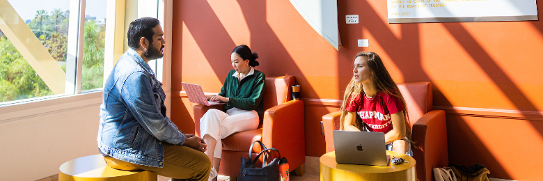 Three Chapman University students sit in lounge area on campus with their laptops