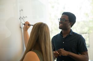 Two students draw a molecular formula on a whiteboard.