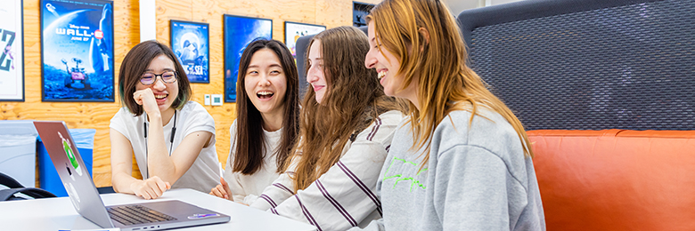 group of female students sitting down in front of a computer smiling and laughing