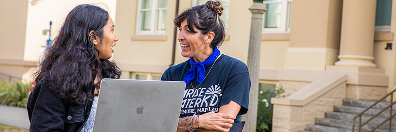 two women talking outside with computer in hand